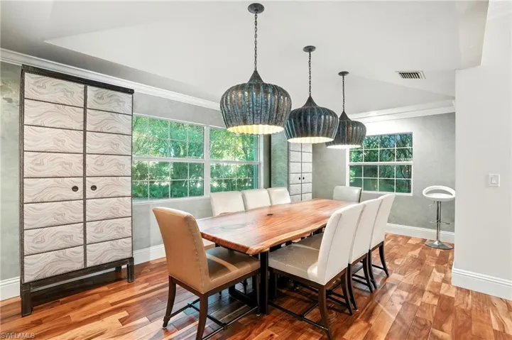 Dining room with ornamental molding, light wood-style flooring, and vaulted ceiling - Virtually Edited Image