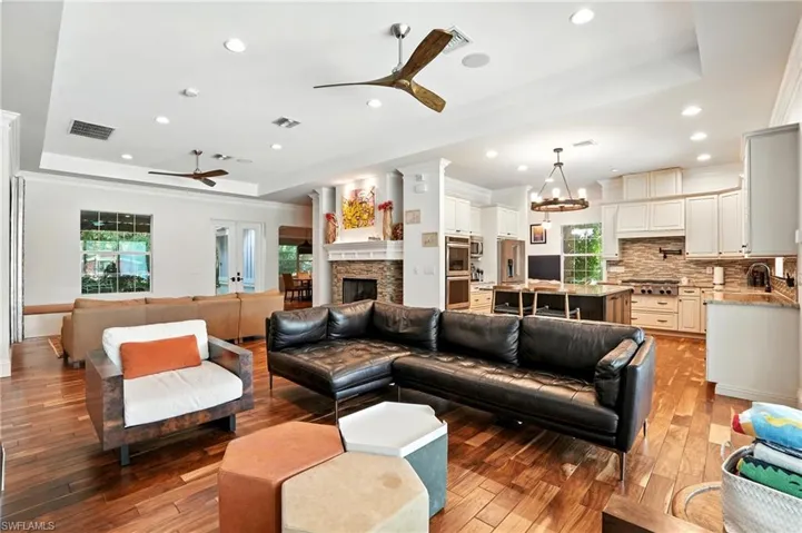 Living area with a raised ceiling, a fireplace, a ceiling fan, hardwood / wood-style floors, and recessed lighting - Virtually Edited Image