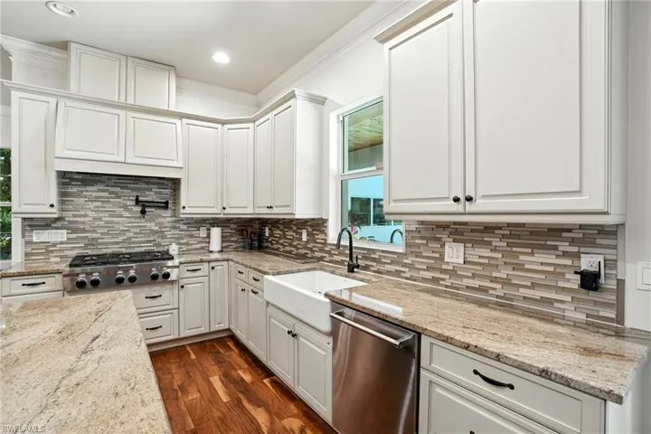 Kitchen with stainless steel appliances, white cabinets, ornamental molding, dark wood-type flooring, and light stone countertops - Virtually Edited Image