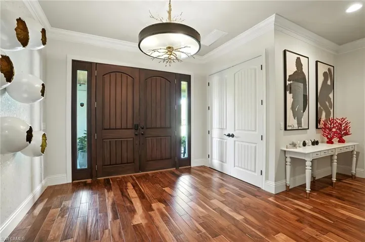 Foyer entrance with crown molding, dark wood finished floors, and a chandelier - Virtually Edited Image