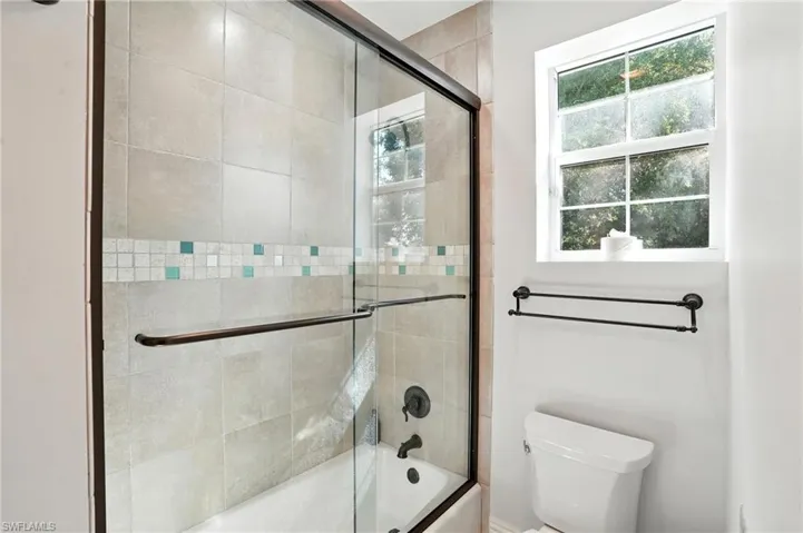 Bathroom featuring combined bath / shower with glass door and healthy amount of natural light - Virtually Edited Image