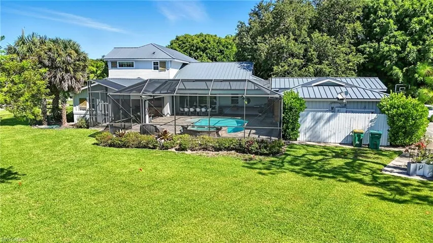 Back of house with a sunroom, a metal roof, glass enclosure, and a lawn - Virtually Edited Image