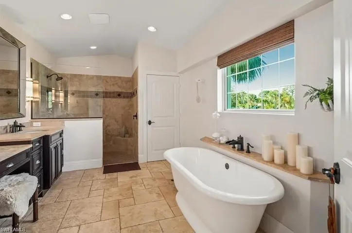 Full bathroom with a freestanding tub, vanity, vaulted ceiling, a walk in shower, and recessed lighting - Virtually Edited Image