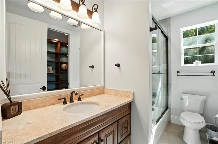 Full bath with enclosed tub / shower combo, vanity, and light tile patterned floors - Virtually Edited Image