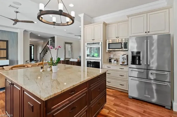 Kitchen featuring a chandelier, appliances with stainless steel finishes, open floor plan, light stone countertops, and light wood-style flooring - Virtually Edited Image