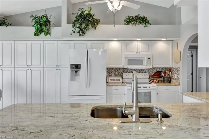 Kitchen with backsplash, light stone countertops, white cabinets, and white appliances