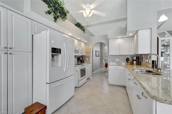 Kitchen with white cabinetry, sink, backsplash, white appliances, and light tile patterned floors