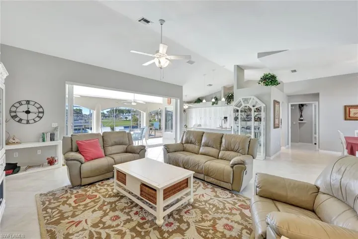 Living room with ceiling fan, light tile patterned flooring, and lofted ceiling