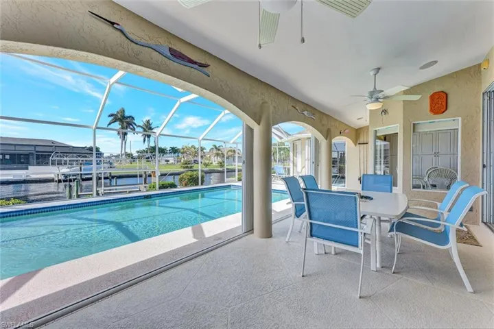 View of swimming pool with glass enclosure, ceiling fan, a patio area, and a water view