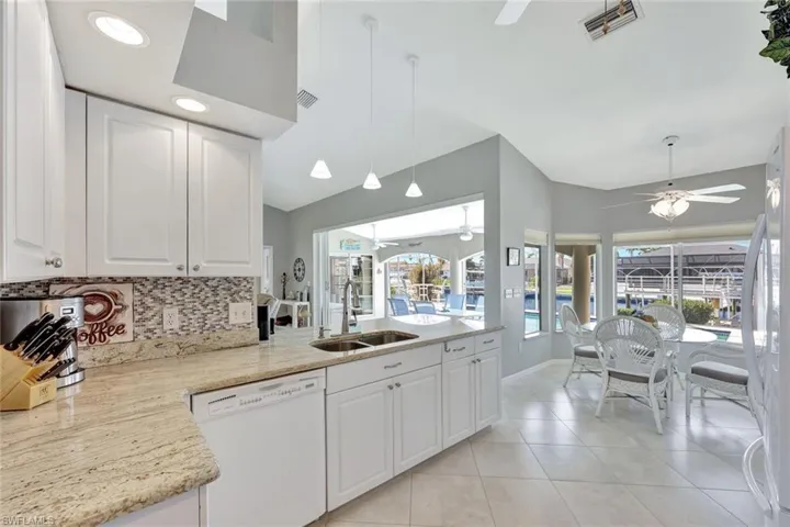 Kitchen featuring dishwasher, white cabinets, light stone counters, and sink
