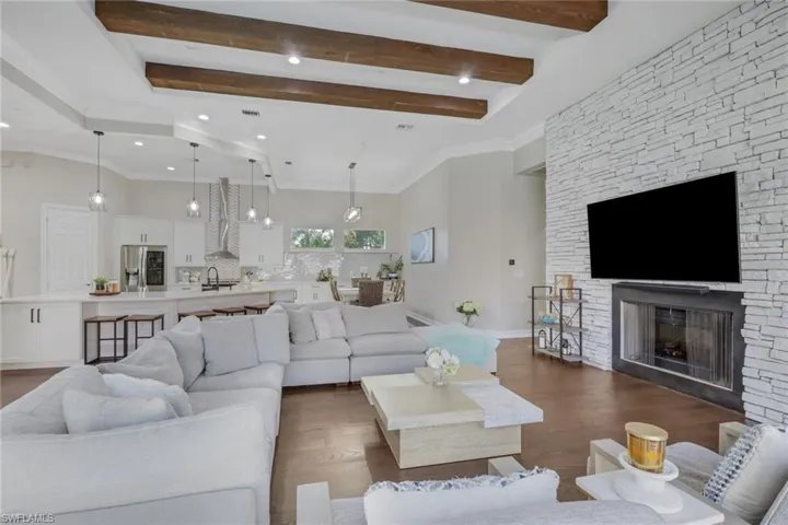Living room with beam ceiling, a stone fireplace, wood finished floors, and crown molding
