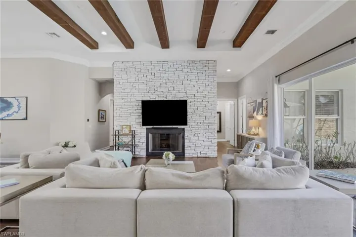 Living room with beamed ceiling, a stone fireplace, crown molding, recessed lighting, and wood finished floors