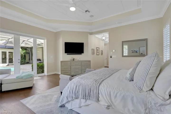 Bedroom featuring wood-type flooring, a raised ceiling, access to exterior, crown molding, and ceiling fan