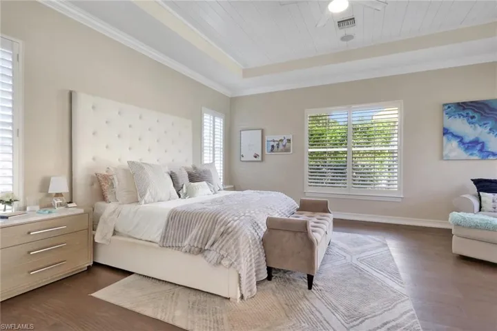 Bedroom with dark wood-style floors, ornamental molding, wood ceiling, ceiling fan, and a raised ceiling