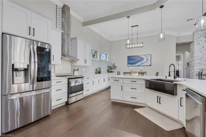 Kitchen with stainless steel appliances, white cabinets, decorative light fixtures, wall chimney range hood, and light stone countertops