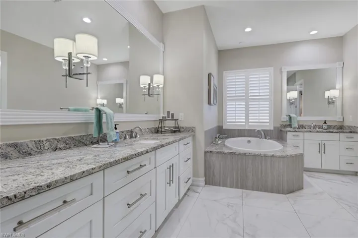 Full bath featuring two vanities, a garden tub, light marble finish flooring, and recessed lighting