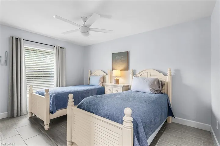 Bedroom featuring two slatted-wood beds, a window with blinds and drapes, a ceiling fan, and tile flooring
