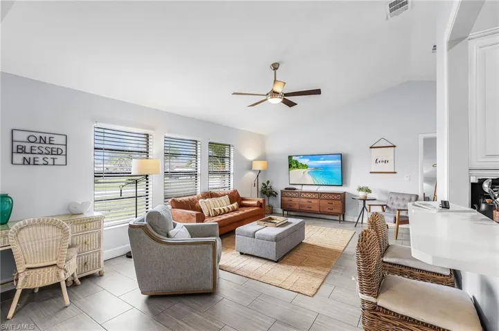 Vaulted ceiling living area featuring tile flooring, ceiling fan, and multiple windows