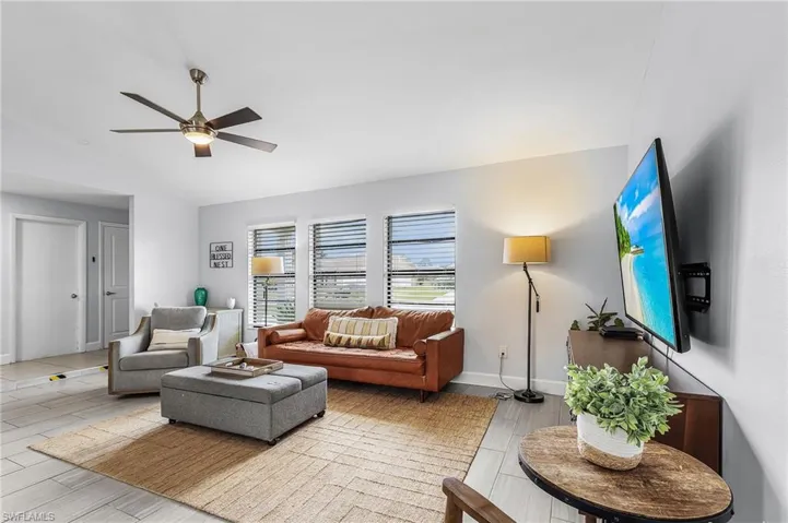 Bright living area featuring wood-finish flooring, a contemporary ceiling fan, and multiple windows with blinds