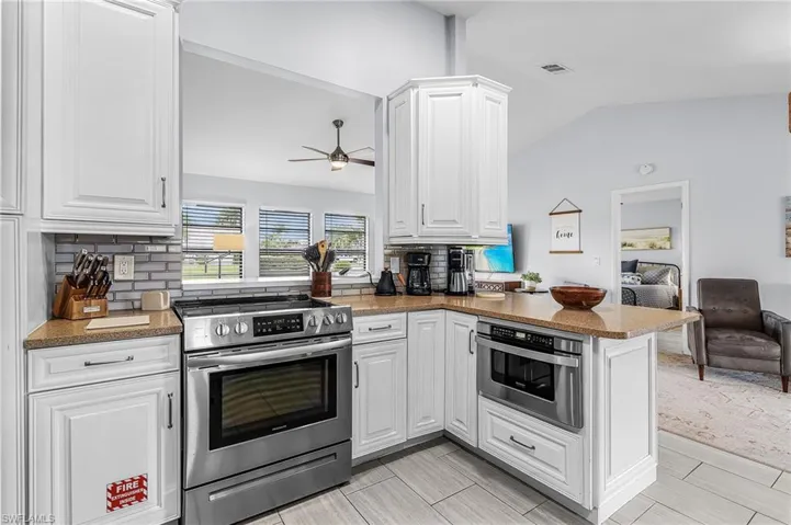 Kitchen featuring white cabinetry, stainless steel appliances, speckled countertops, a subway tile backsplash, and a pass-through window to the adjacent room