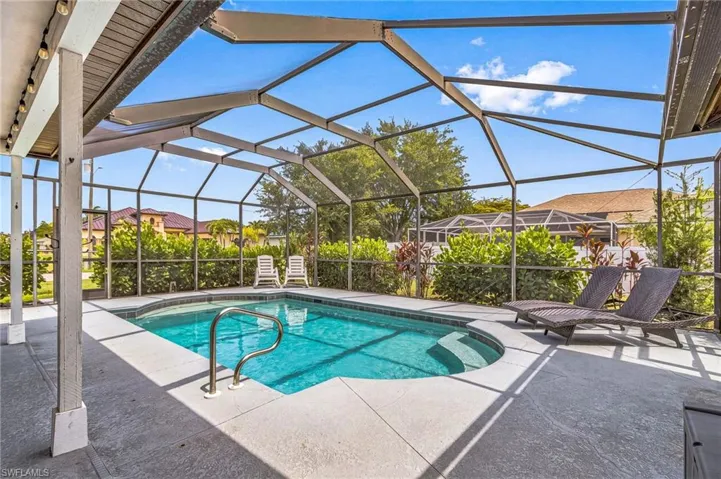 Screened outdoor pool area featuring a rectangular pool with integrated steps, concrete decking, and mature landscaping