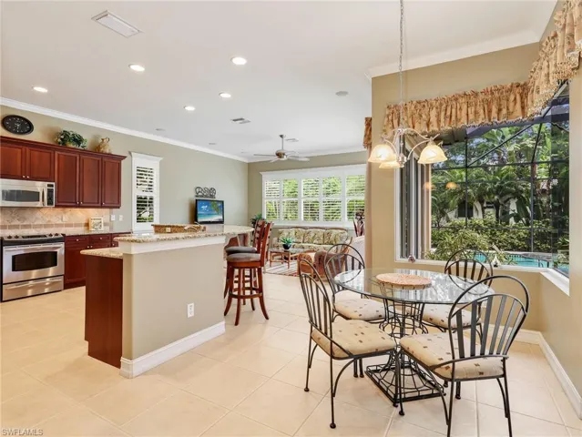 Kitchen with 42" Cabinetry, Stainless Steel Appliances & Breakfast Bar, Eat-In Kitchen with Large Frameless Window with Pool View, & Family Room with Plantation Shutters & Sliders Leading to the Screened-In Lanai