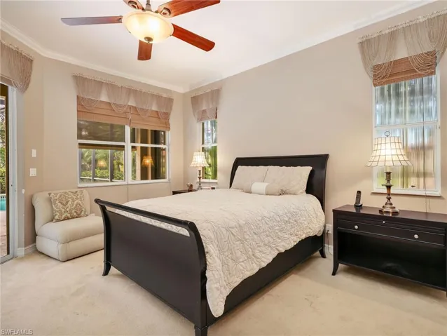Primary Bedroom with Crown Molding, Window Coverings, Ceiling Fan, & Sliders Leading to the Screened-In Lanai with a Pool View