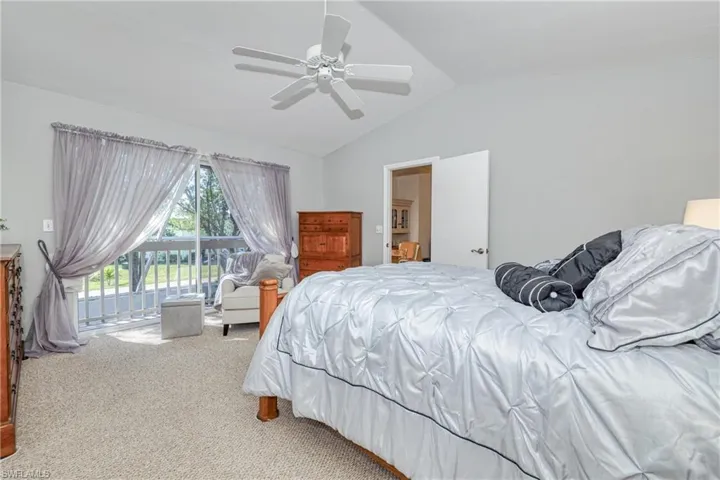 Carpeted bedroom featuring ceiling fan, vaulted ceiling, and access to outside