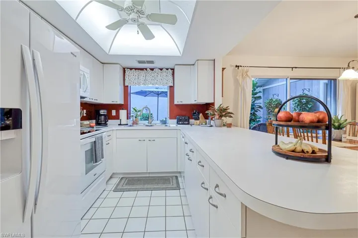Kitchen with sink, white cabinets, light tile patterned floors, kitchen peninsula, and white appliances