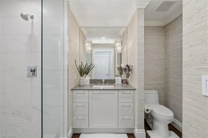 Bathroom featuring a glass-enclosed shower with white tiled walls, a single vanity with a light gray countertop and white cabinetry, a built-in toilet, and textured wall coverings throughout
