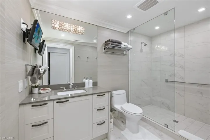 Bathroom featuring a glass-enclosed shower, white vanity with a grey countertop, integrated sink, and large wall mirror