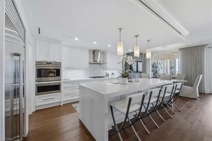 Gourmet kitchen featuring a waterfall island with seating, integrated stainless steel appliances, white shaker cabinetry, and a full-height tile backsplash