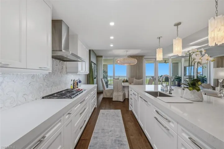 Gourmet kitchen featuring white shaker cabinetry, an integrated gas cooktop, decorative backsplash, a stainless steel range hood, and wood-finish flooring