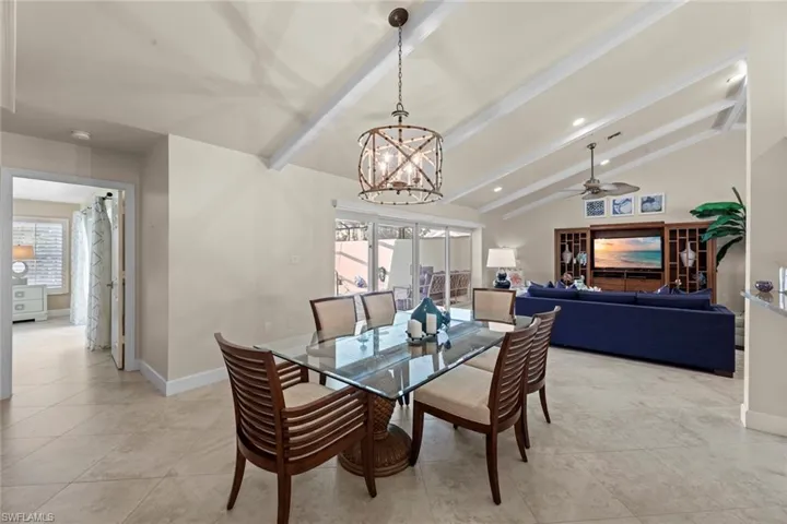 Dining room with vaulted ceiling with beams, light tile floors, and ceiling fan with notable chandelier