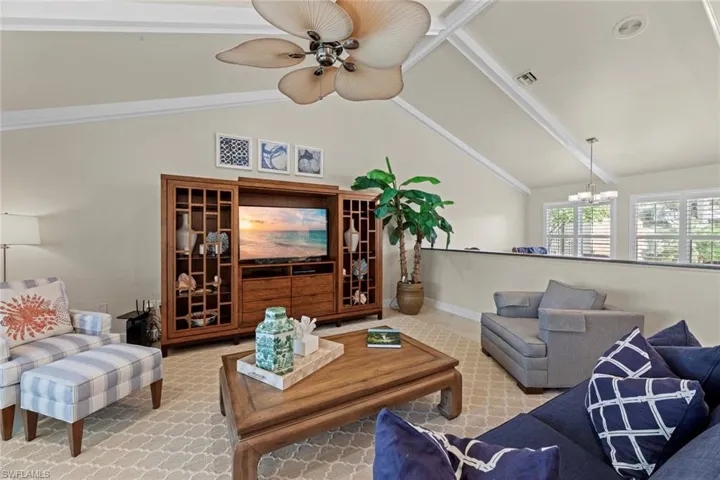 Living room with ceiling fan with notable chandelier and vaulted ceiling with beams