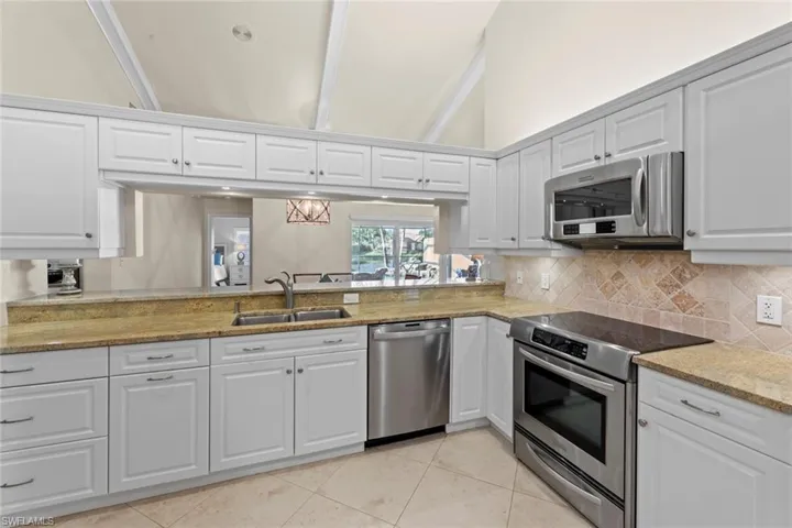 Kitchen with beamed ceiling, sink, white cabinetry, and appliances with stainless steel finishes