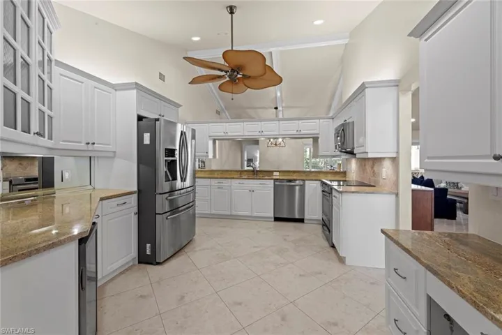 Kitchen with ceiling fan, stainless steel appliances, backsplash, light tile floors, and white cabinetry