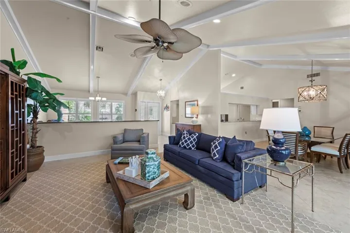 Living room with beamed ceiling, ceiling fan with notable chandelier, and high vaulted ceiling