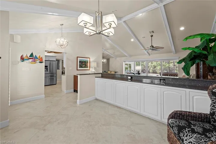 Kitchen with hanging light fixtures, vaulted ceiling with beams, white cabinets, and stainless steel fridge with ice dispenser