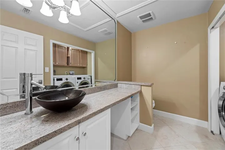 Bathroom with washing machine and dryer, tile flooring, vanity with extensive cabinet space, and toilet