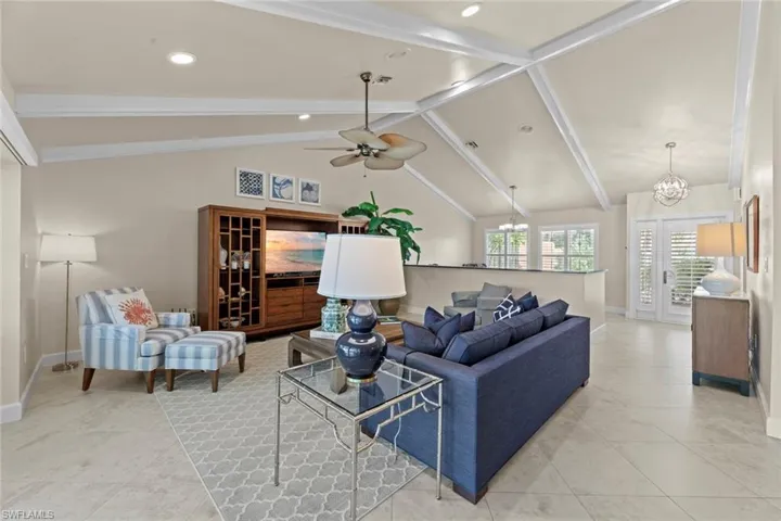 Tiled living room with beam ceiling, high vaulted ceiling, french doors, and ceiling fan with notable chandelier