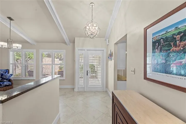 Tiled foyer entrance featuring beamed ceiling, a notable chandelier, and crown molding