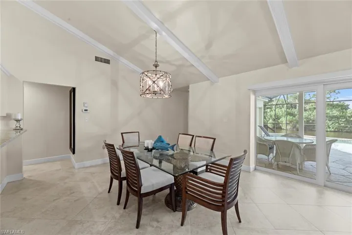 Tiled dining space featuring vaulted ceiling with beams and a chandelier