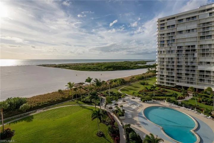 Expansive oceanfront setting featuring a sandy beach, mature palm trees, a resort-style swimming pool, and a high-rise condominium building