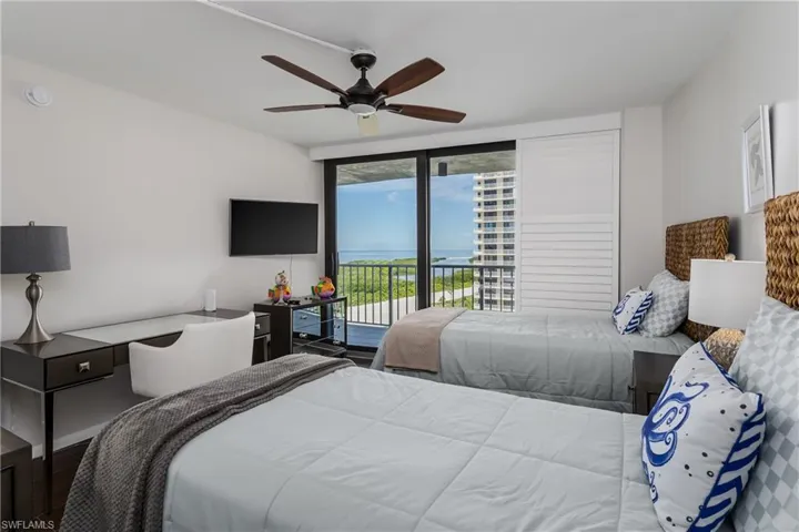 Sliding glass doors to a balcony, desk with a built-in drawer, and wall-mounted television
