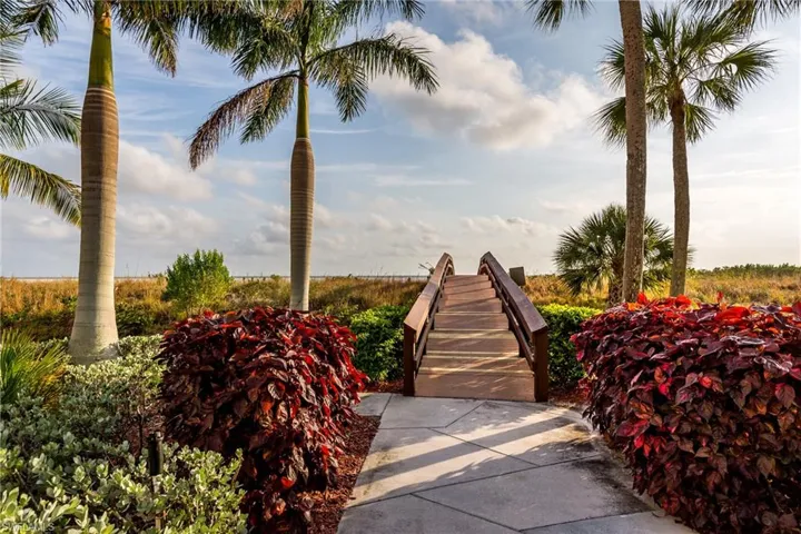 To the Beach wood-finish elevated walkway with railings, surrounded by lush landscaping, mature palm trees, and concrete paver pathway