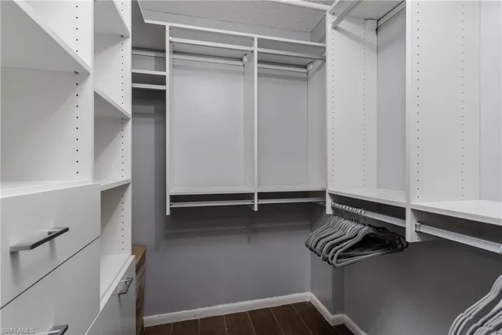 Custom closet organization system featuring white shelving, multiple hanging rods, built-in drawers with modern pulls, and wood-finish flooring