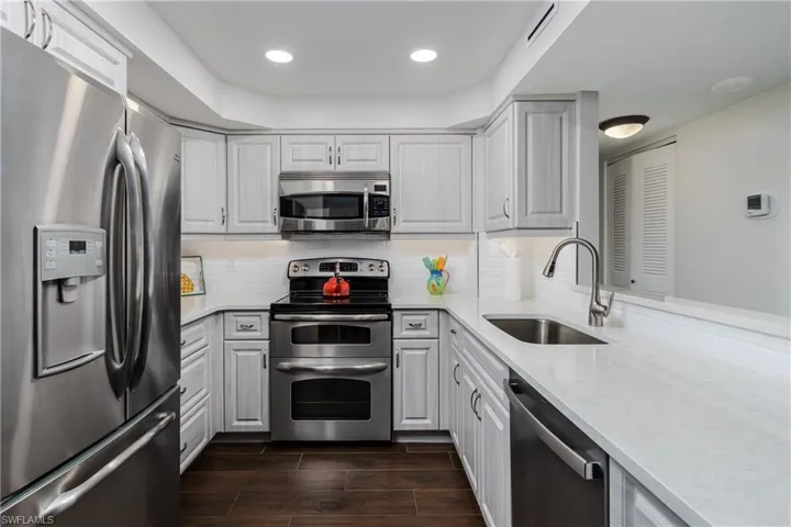 Kitchen with stainless steel appliances, white cabinetry, solid surface countertops, and wood-finish flooring