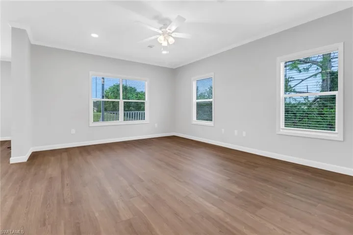 Living room featuring laminated floors, a wealth of natural light, crown molding, and ceiling fan