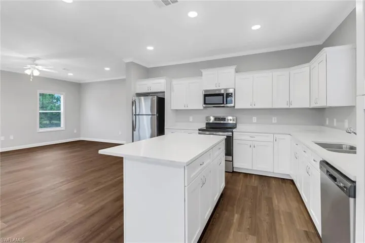 Kitchen with island, sink, stainless steel appliances, laminated floors and white cabinets